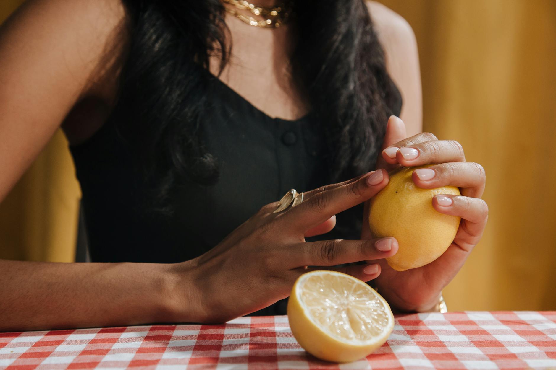 A woman with dark hair holding a fresh yellow lemon at a dining table, symbolizing anticipation and readiness.