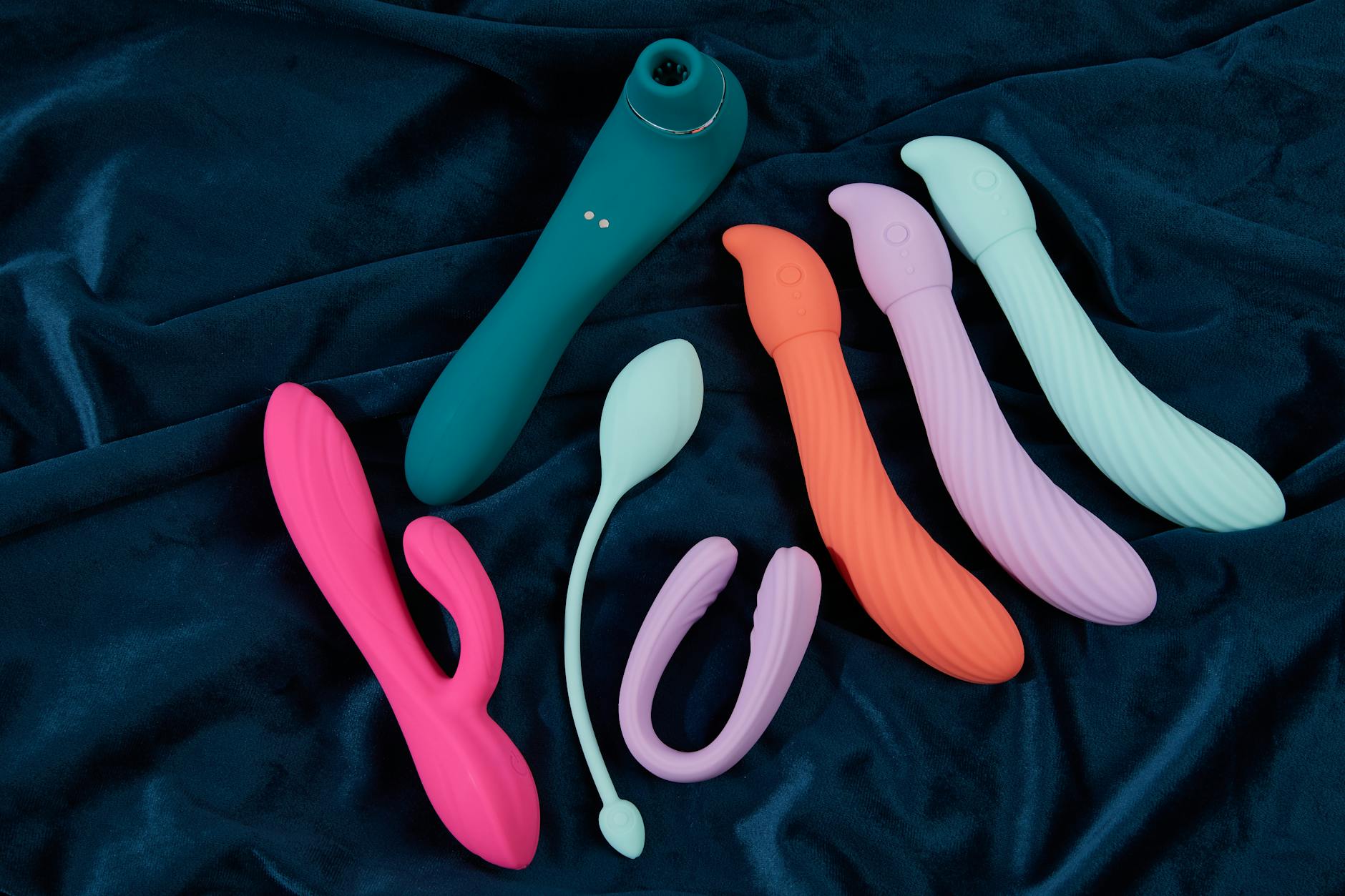 Collection of colorful vibrators arranged on dark fabric, showcasing various shapes and textures