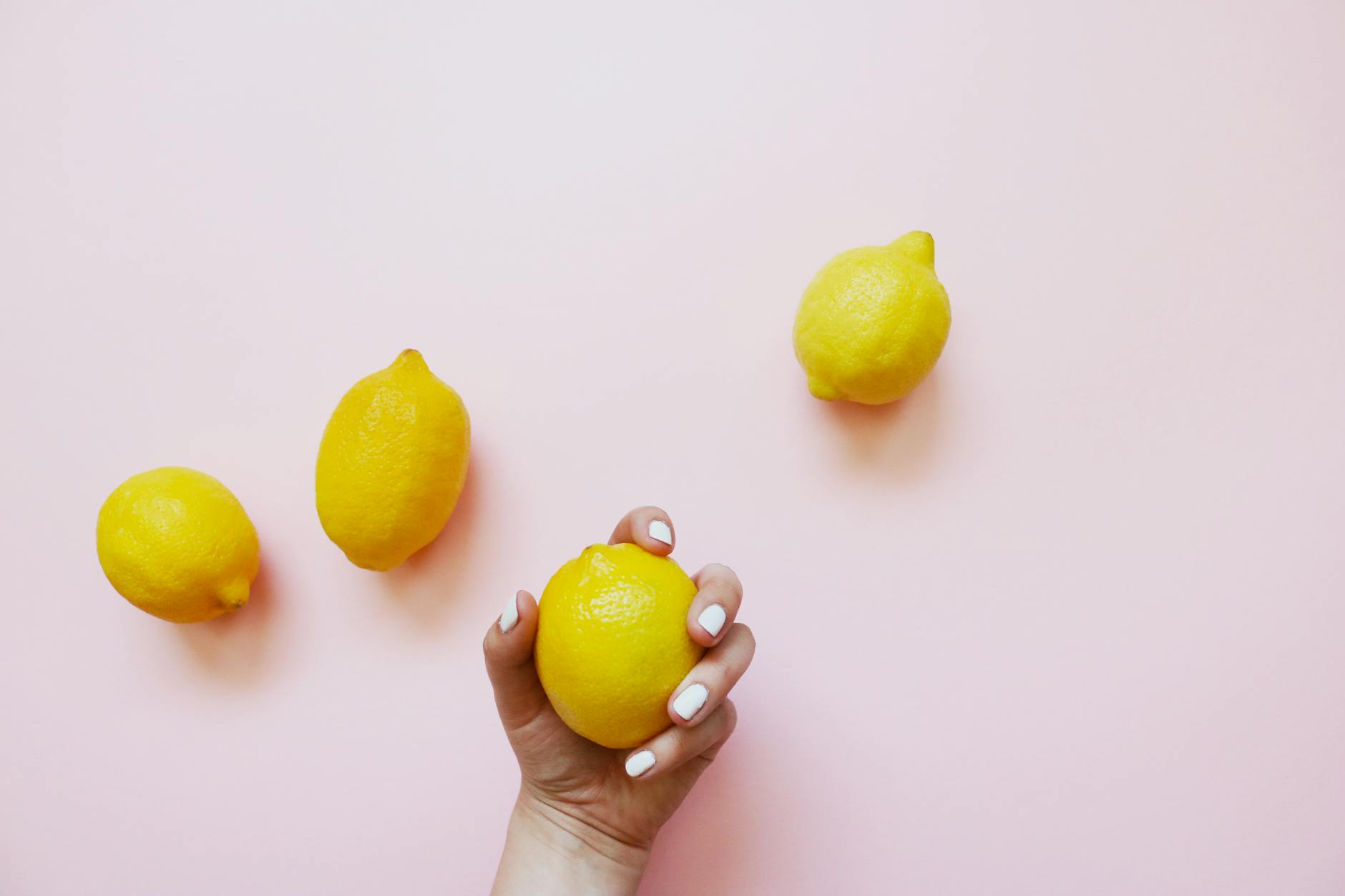 A hand holding a bright lemon on a soft pink background, symbolizing intimacy and connection across distance.