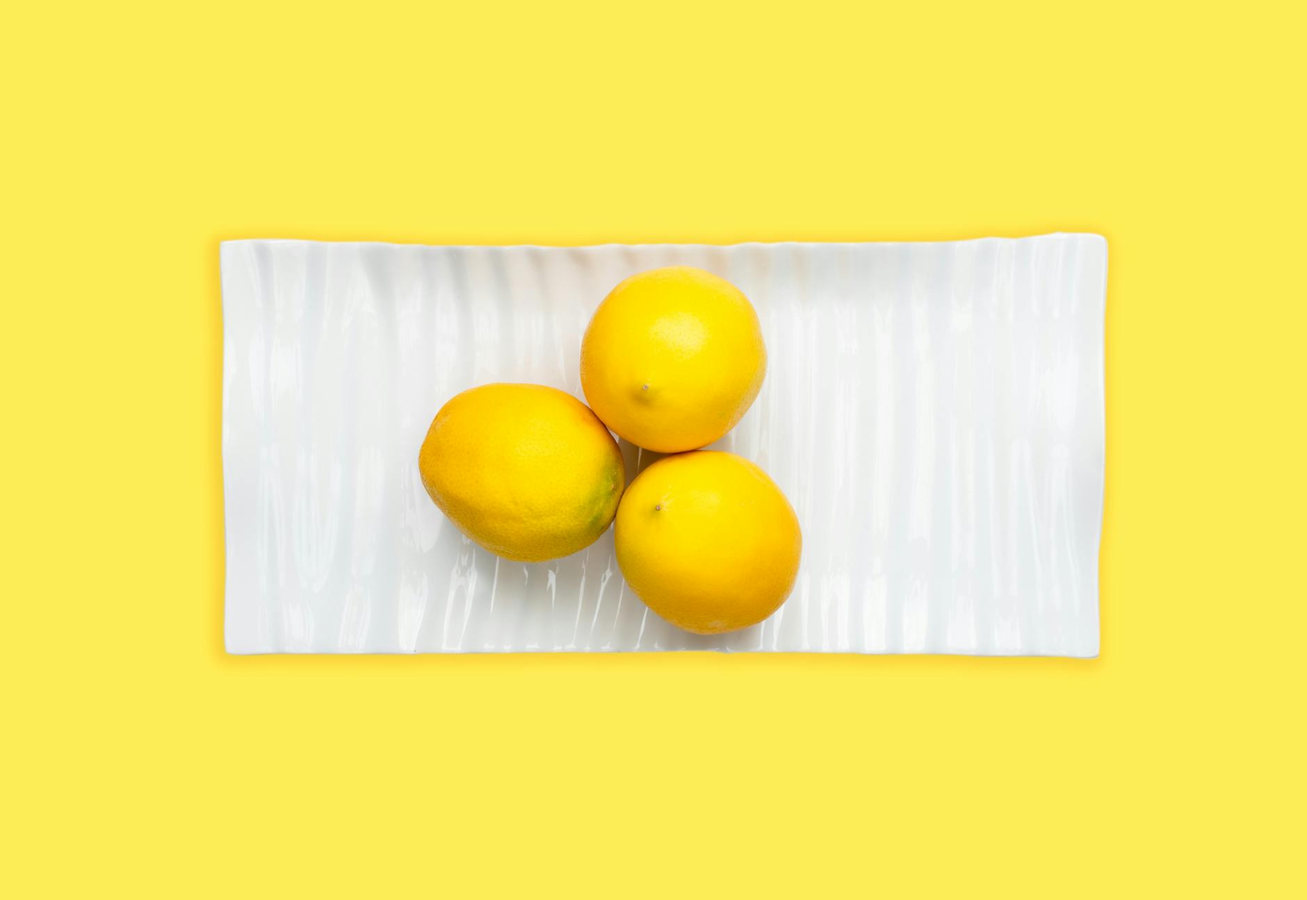 Fresh lemons arranged on white plate with vibrant yellow background, representing clarity and freshness in sexual wellness