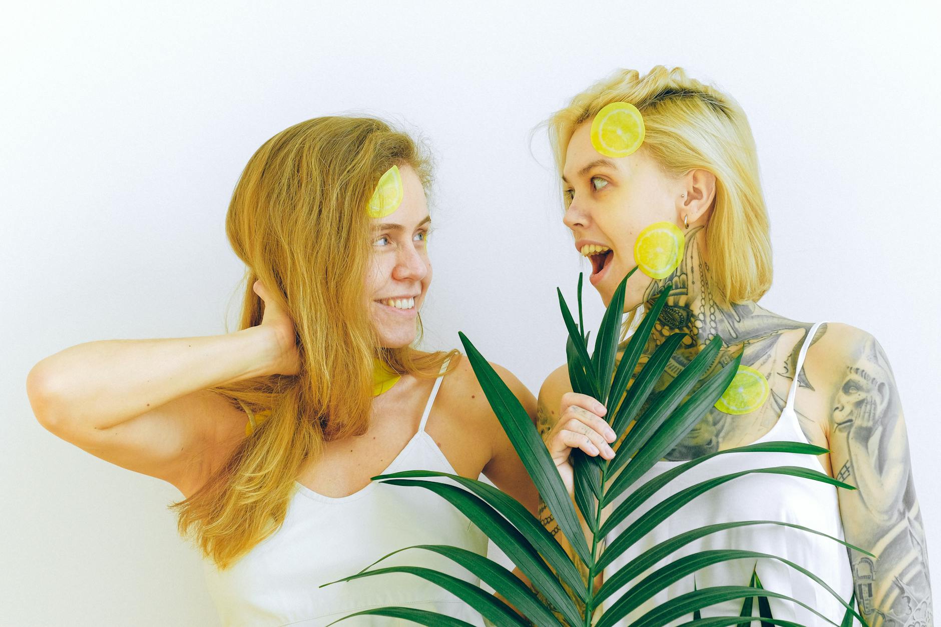 Two women smiling with lemon slices, expressing joy and confidence in a bright indoor setting.