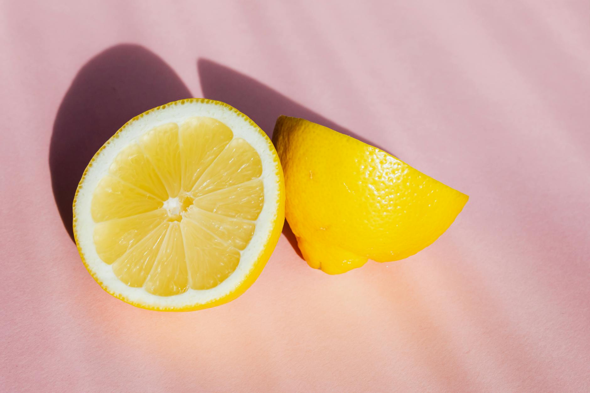 Fresh lemon halves arranged on a pink background in natural sunlight