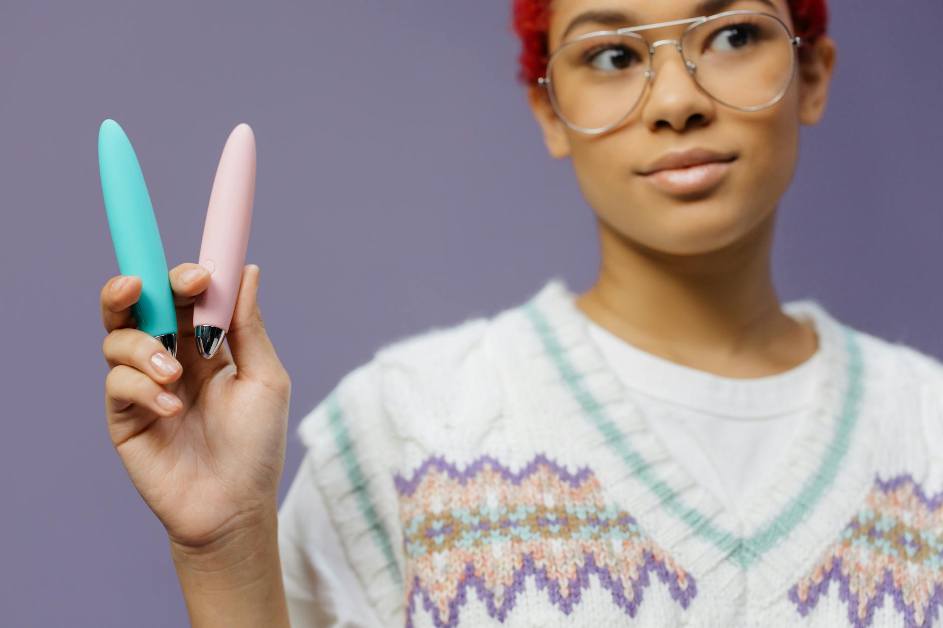 A young woman holding two colorful vibrators against a purple background